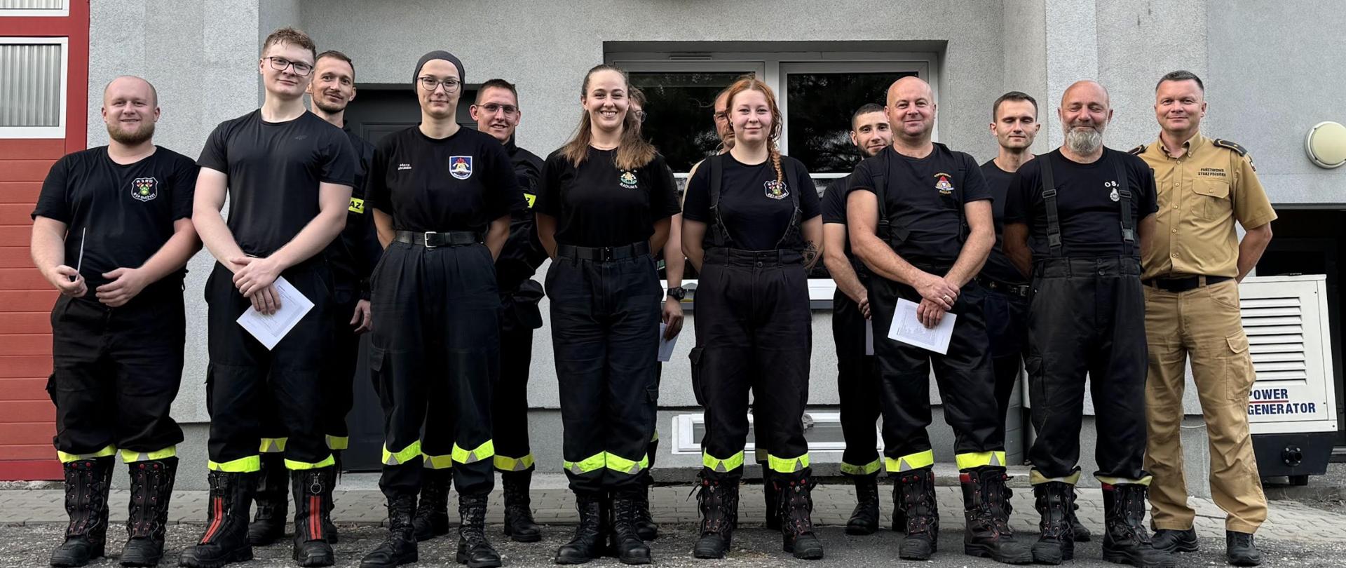 Zdjęcie grupowe absolwentów szkolenia podstawowego OSP. W tle budynek JRG Rydułtowy.