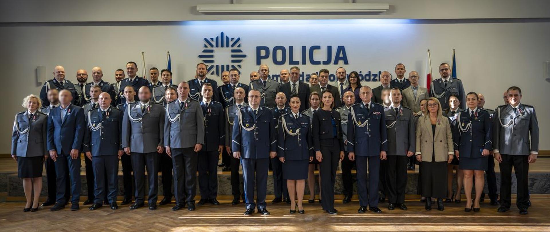 grupa kilkudziesięciu osób - kobiet i mężczyzn w mundurach stoją w sali na tl;e napisu Policja