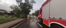 Powalone drzewo na drodze które usuwają strażacy przy pomocy pił spalinowych