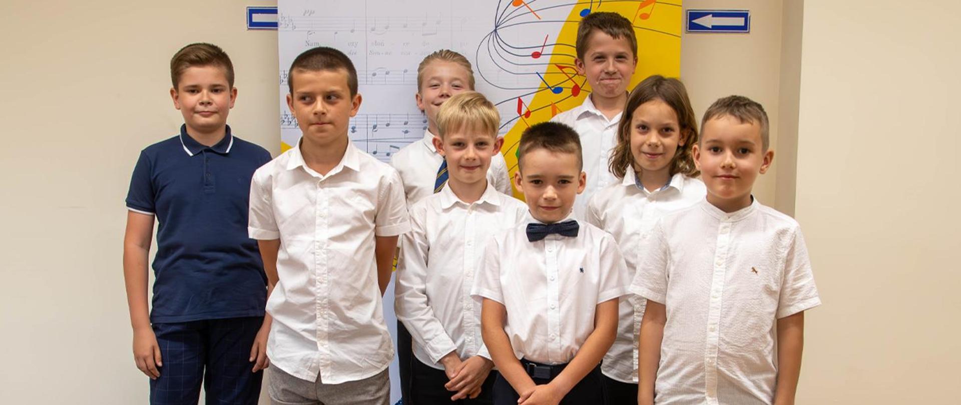 Na zdjęciu 8 chłopców stojących na tle baneru szkolnego.