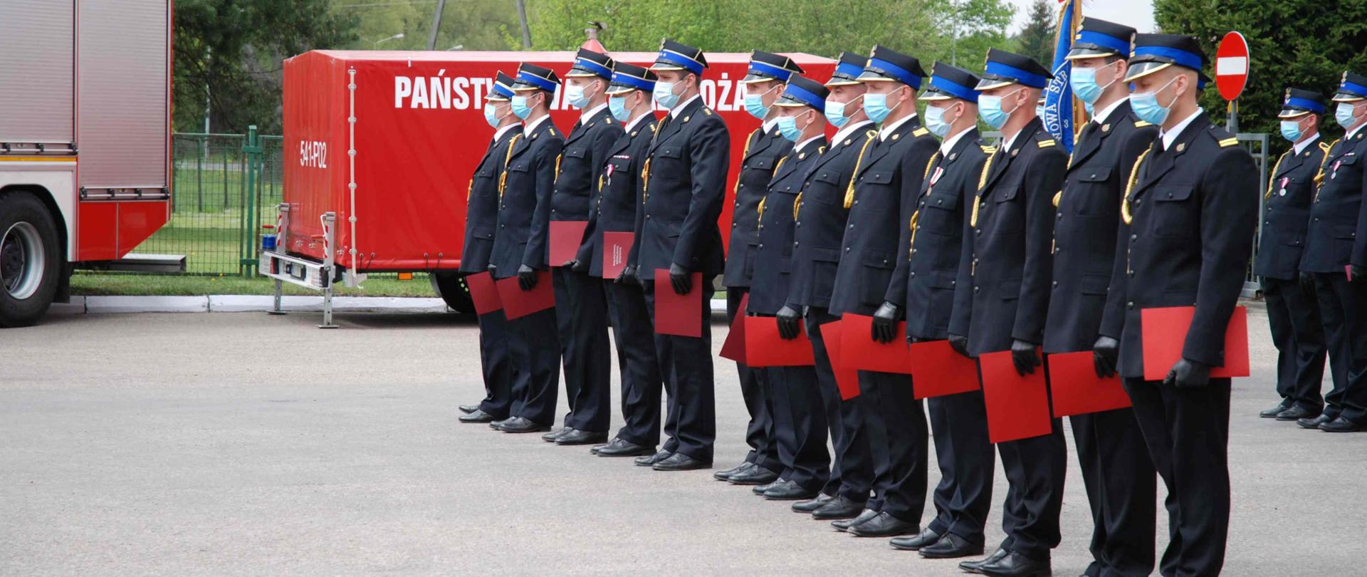 Strażacy stojący w szeregu w trakcie wręczania odznaczeń.