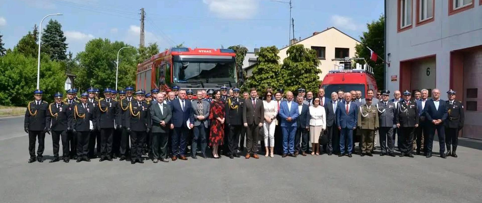 uczestnicy uroczystości pozują do zdjęcia grupowego w tle dwa samochody pożarnicze