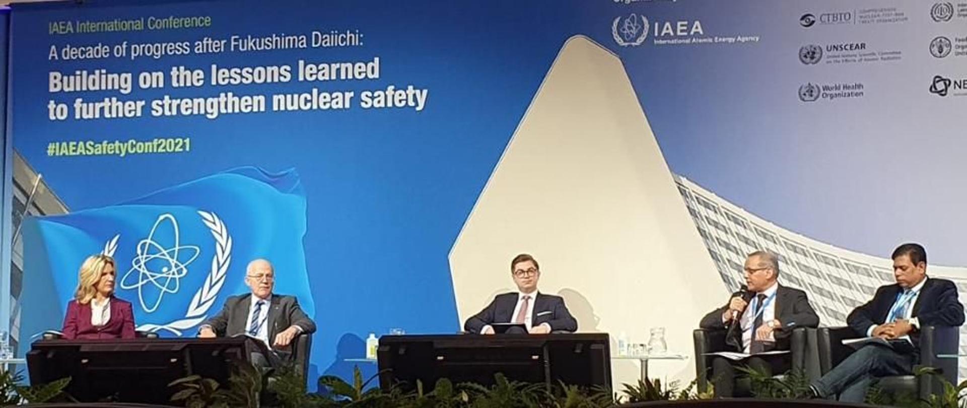 IAEA conference on lessons learned from the Fukushima nuclear disaster. Discussion panel - five experts sit on chairs on the stage. Behind them, a large poster with the words 'Building on the lessons learned to further strength nuclear safety.