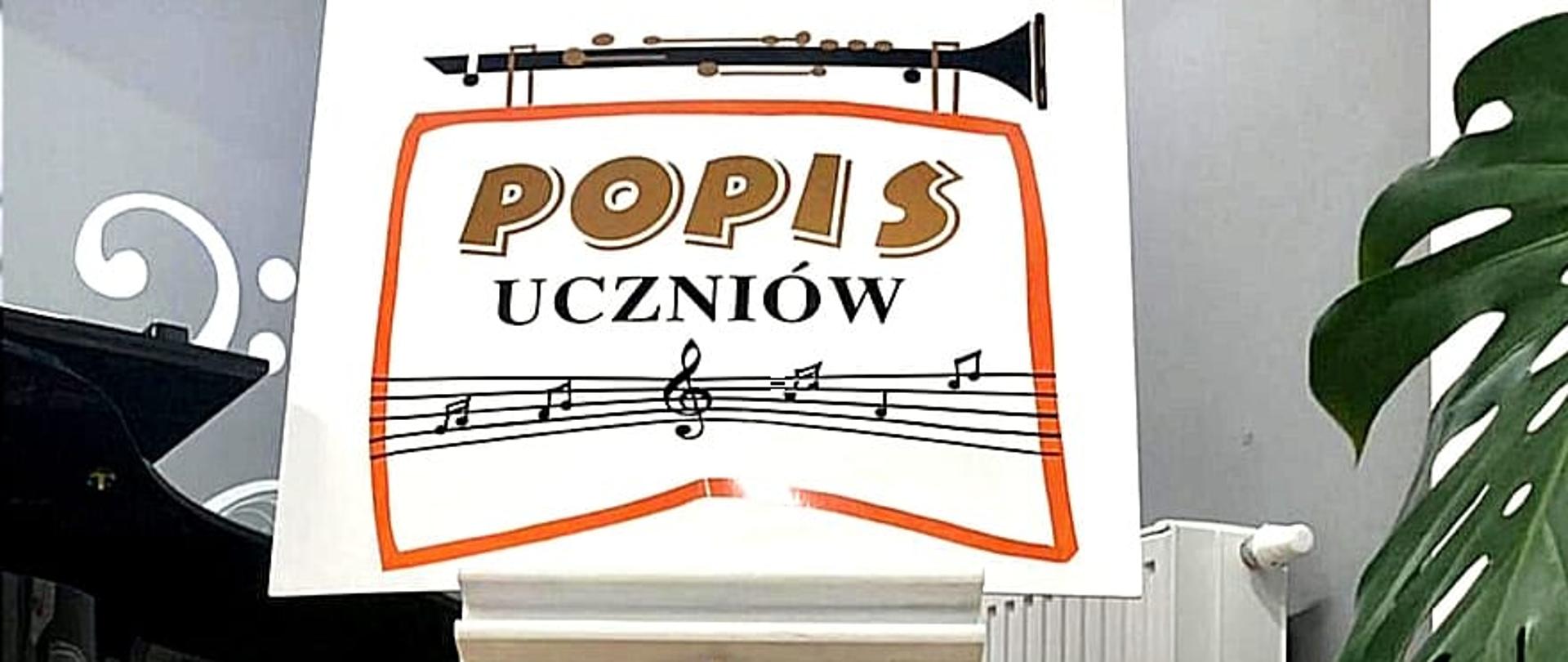 Zdjecie przedstawia plakat z napisem Popis uczniów oraz wesołych świat w tle widac fortepian