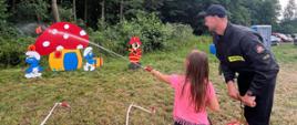 „Zażynki” w Dzierzbach Włościańskich 14.07.2024 - na zdjęciu dziecko na trawie przed lasem polewa wodą z hydronetki demonstracyjne zestawy do gaszenia pożarów - chata smerfów