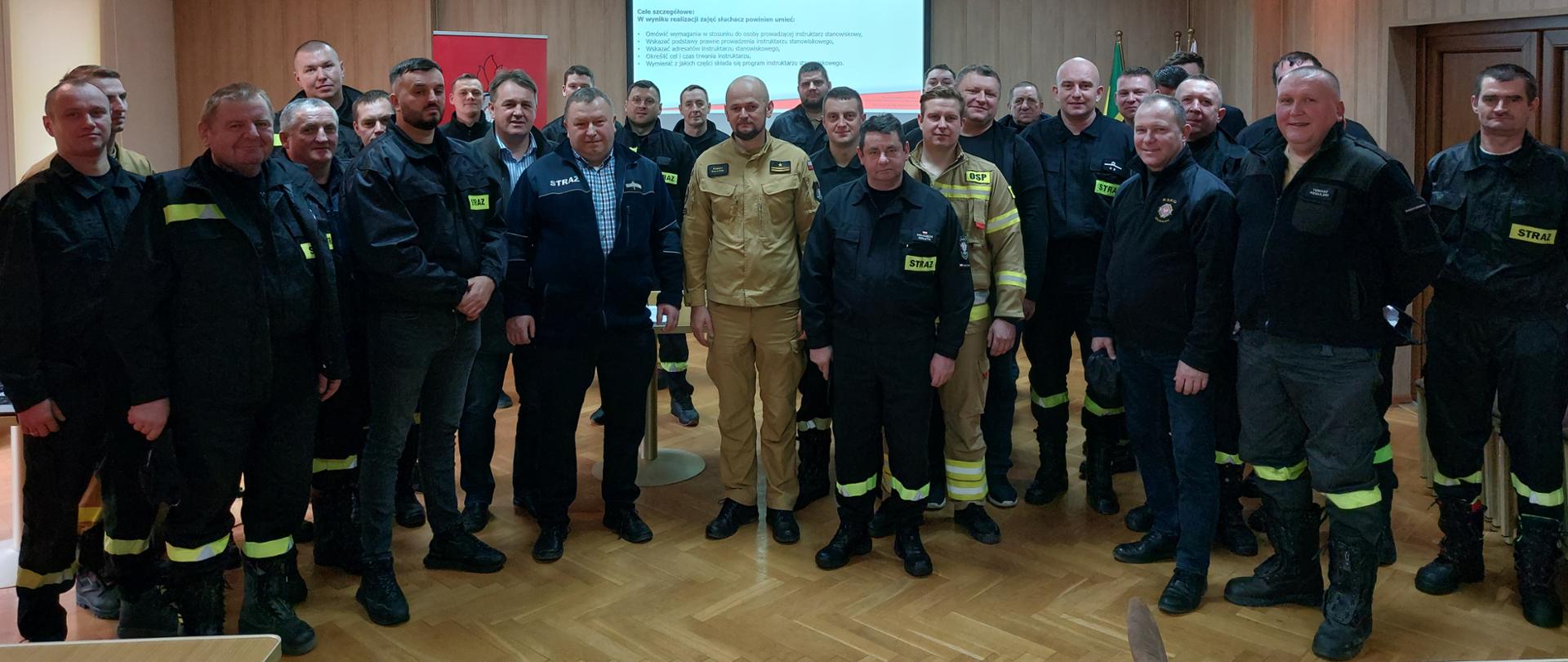 Zdjęcie przedstawia druhów Ochotniczych Straży Pożarnych a w tle wisi ekran multimedialny