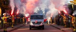 Nowy samochód typu mikrobus Renault Trafic jedzie przez szpaler strażaków, którzy w ręku trzymają odpalone race.