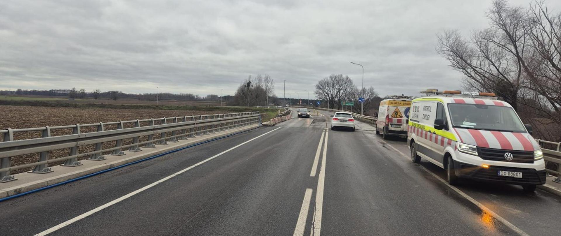 Pierwsze samochody poruszające się drogą krajową nr 94 dwoma pasami ruchu. Pochmurny dzień. Na pasie awaryjnym widoczne pojazdy służby drogowej.