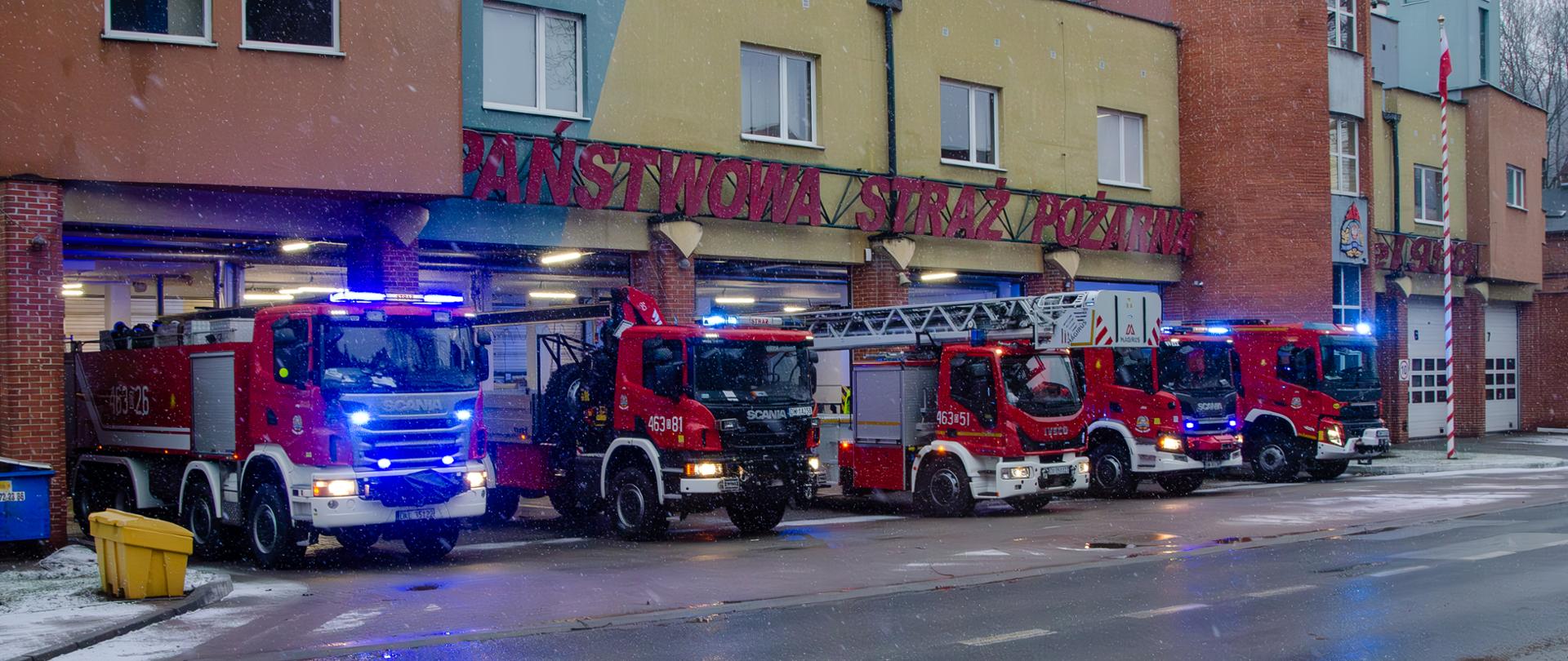 Budynek Jednostki Ratowniczo-Gaśniczej w Nowej Rudzie. Przed budynkiem w otwartych pięciu bramach garażowych stoją samochody pożarnicze. 