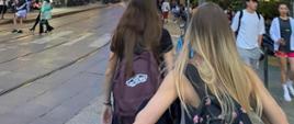 Dwie dziewczyny spacerujące z plecakami wśród tłumu ludzi.