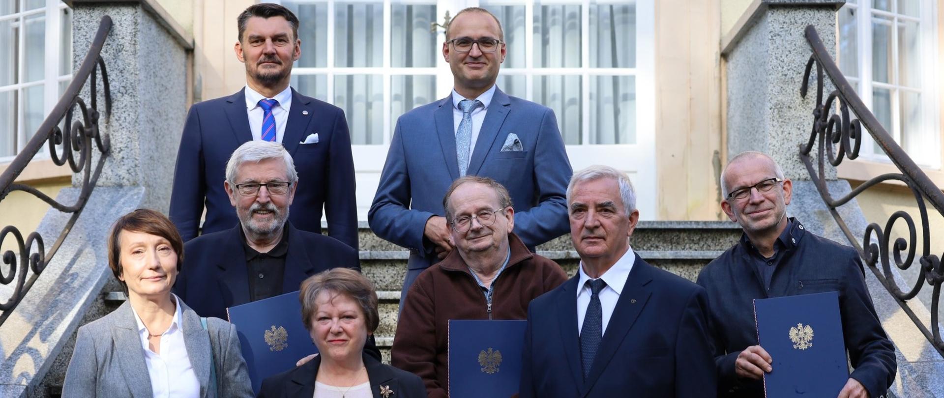 Kilka osób stoi przed budynkiem urzędu, część trzyma nominacje na członków rady