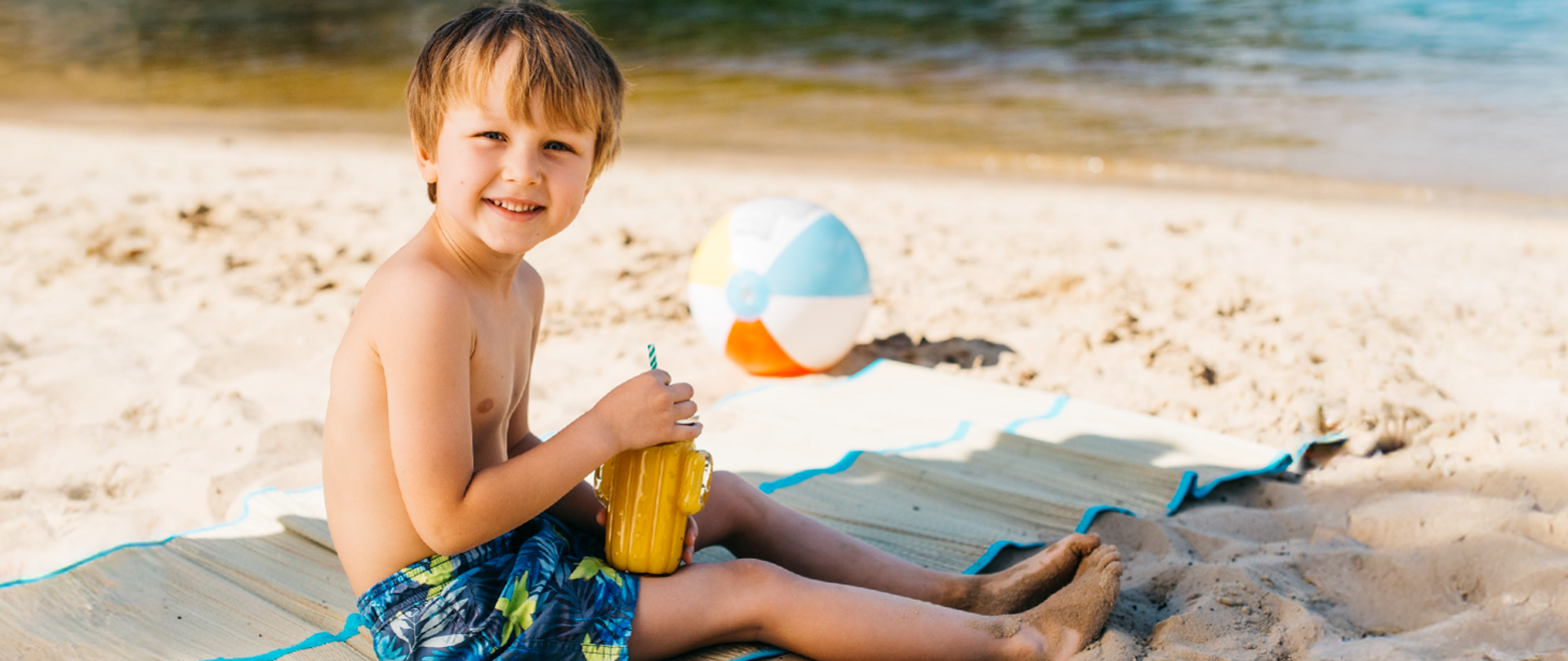 Dzieciak z napojem, siedzi na plaży.