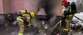 Strażacy gaszą elementy z piwnicy przed budynkiem