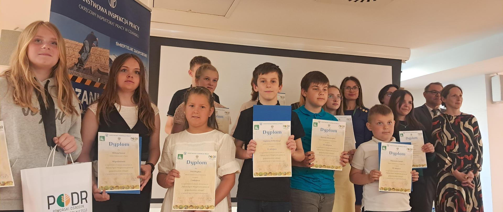 Grupa dzieci z dyplomami z logo KRUS, PIP i PODR