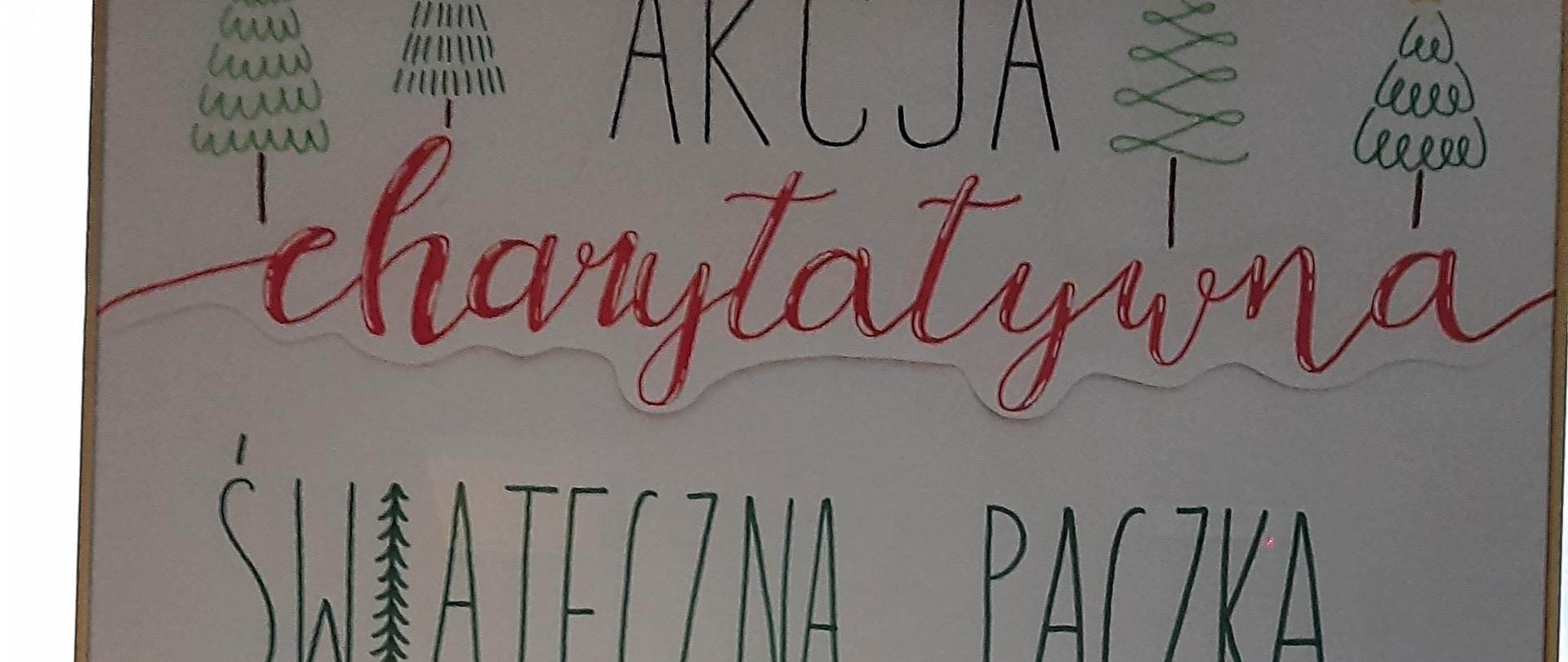 Zdjęcie przedstawia plakat z napisem "Akcja charytatywna "Świąteczna Paczka" dla Karmelitanek Bosych z Dysa. Dary zbieramy do 8 grudnia i przynosimy do pokoju wychowawców.. Na górze plakatu narysowane 4 zielone choinki,, na dole sanie wypełnione kolorowymi prezentami i zwisające 5 okrągłych czerwonych bombek. Plakat oprawiony w fotoramę i ustawiony na drewnianej sztaludze.