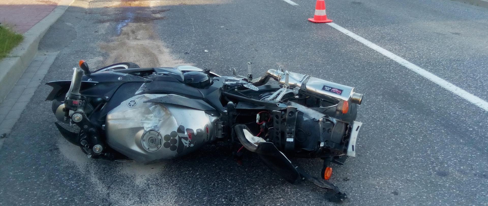 Zdjęcie przedstawia motocykl, który uległ wypadkowi i leży na boku na jezdni