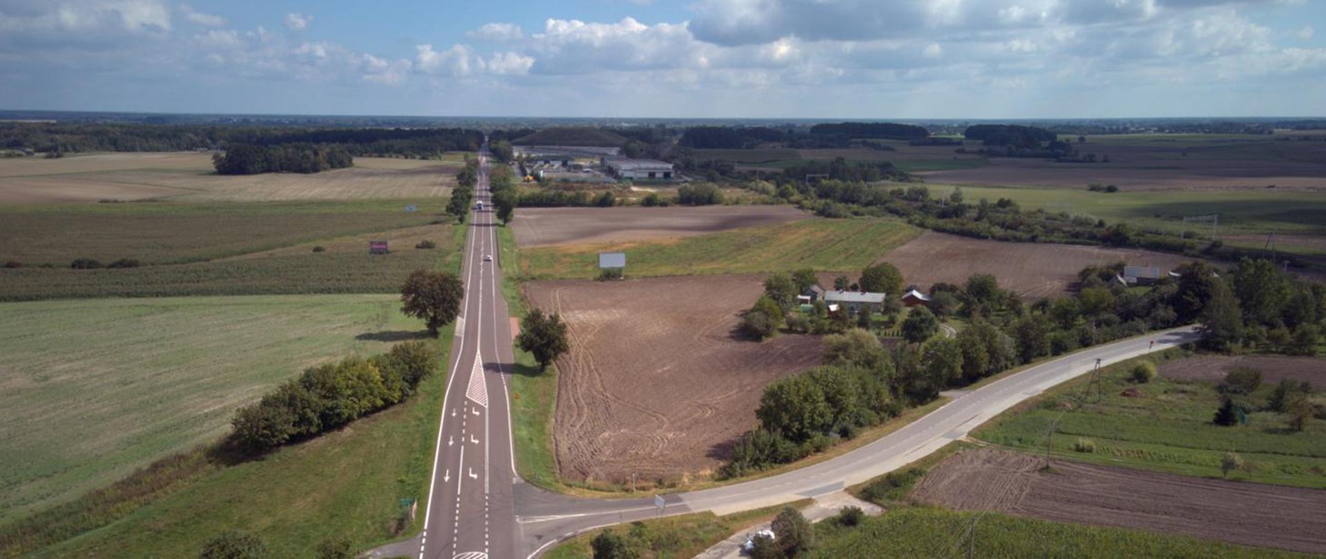 Pogodny dzień, na niebie chmury. Widok z lotu ptaka na drogę biegnącą wśród pól.