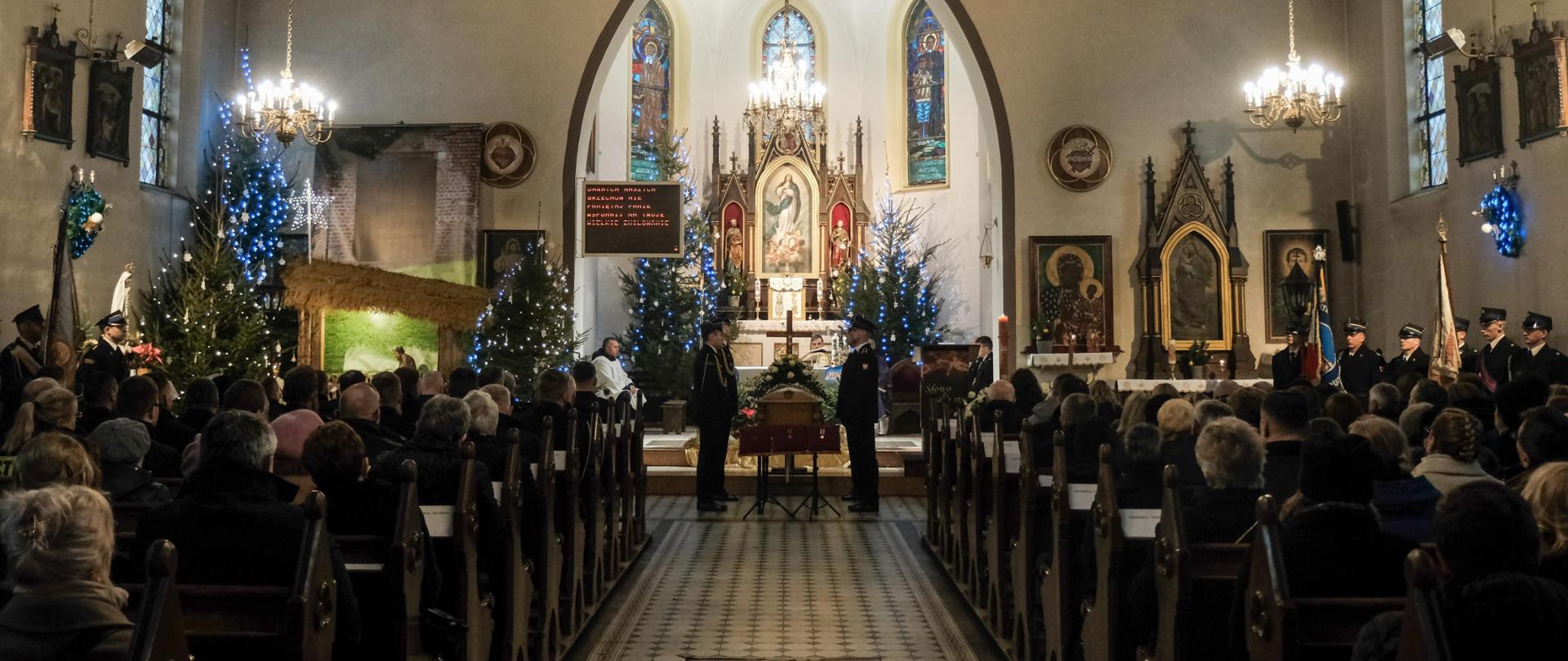 Msza św. pogrzebowa w Kościele Wniebowzięcia Najświętszej Maryi Panny w Debrznie. Przed ołtarzem głównym stoi trumna i czteroosobowy posterunek honorowy w asyście pocztów sztandarowych. Po obu stronach w ławkach siedzą: rodzina i przyjaciele Zmarłego, funkcjonariusze, delegacje władz samorządowych oraz przedstawicieli innych służb i instytucji.