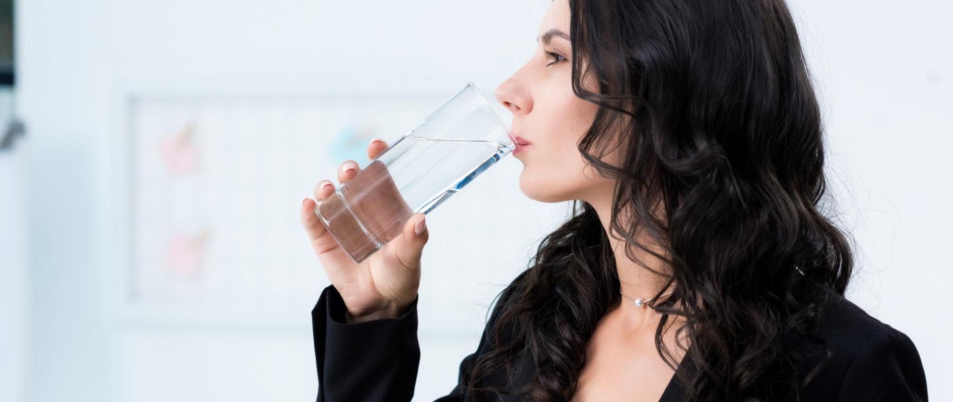 Na zdjęciu jest kobieta pijąca wodę ze szklanki.
