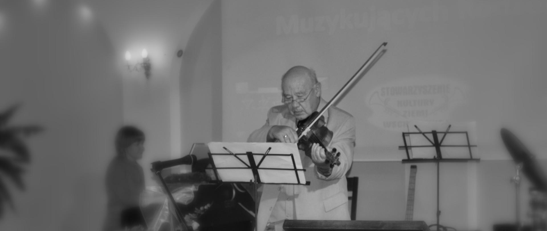 Na zdjęciu widoczny jest Pan Karol Muszkieta grający na skrzypcach. Zdjęcie jest czarno-białe.