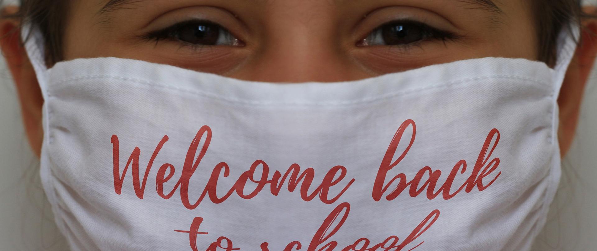 twarz dziewczynki z białą maseczką ochronną na twarzy, na której jest napisane welcome back to school - witaj z powrotem w szkole.