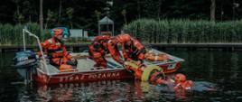 Strażacy na łodzi podczas ćwiczeń wyciągają strażaka z wody na pokład