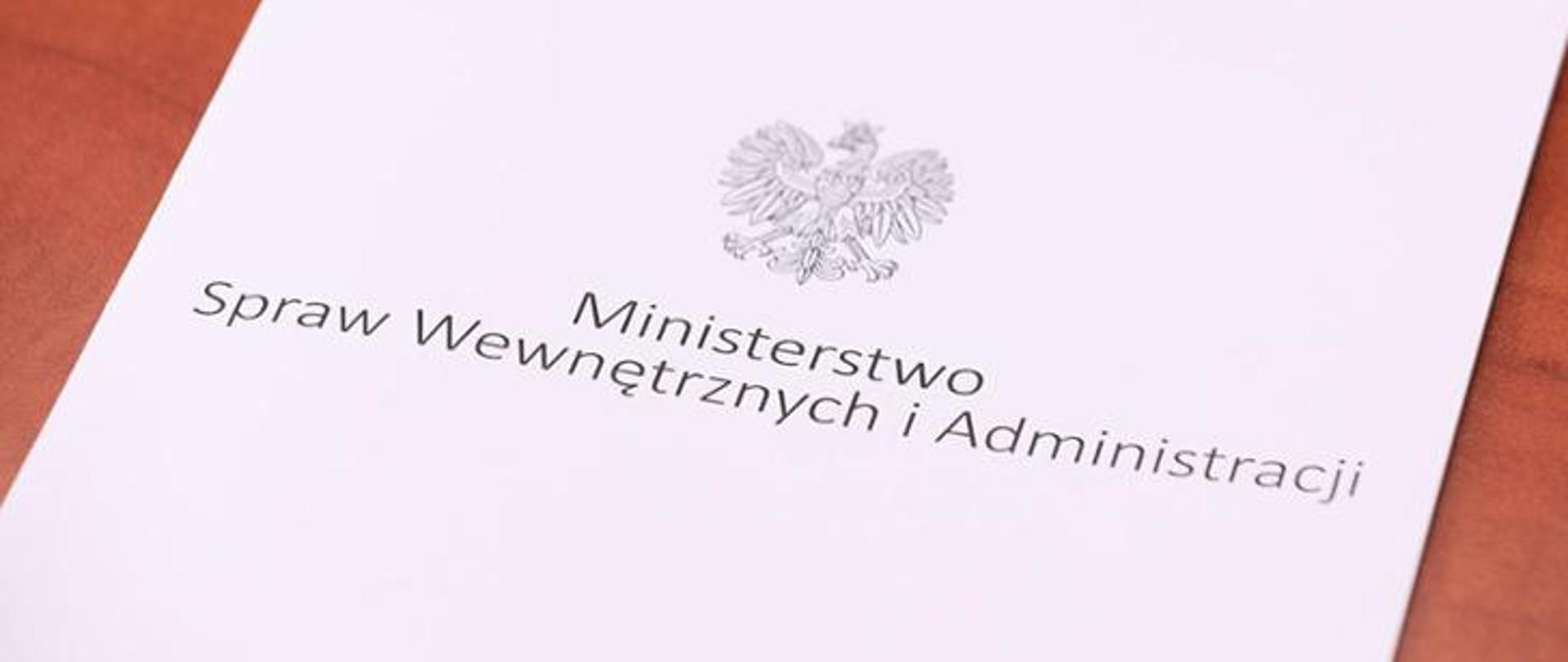 Biała teczka z orzełkiem i napisem: Ministerstwo Spraw Wewnętrznych i Administracji