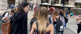 Grupa uśmiechniętych dziewcząt z plecakami w Mediolanie wśród tłumu ludzi.