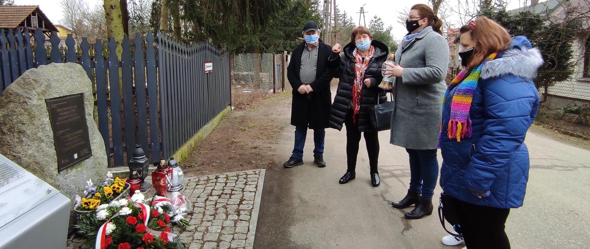 Na zdjęciu znajduje się kilka osób, stoją przed pomnikiem