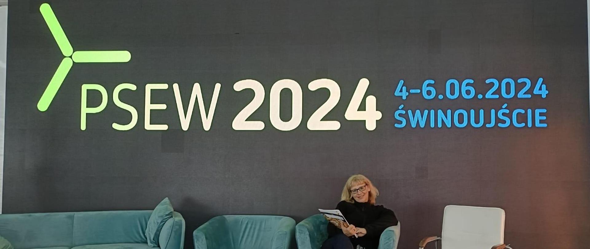 Na tle szarej ściany z napisem: PSEW 2024, 4-6.06.2024 Świnoujście, siedzi uśmiechnięta kobieta,