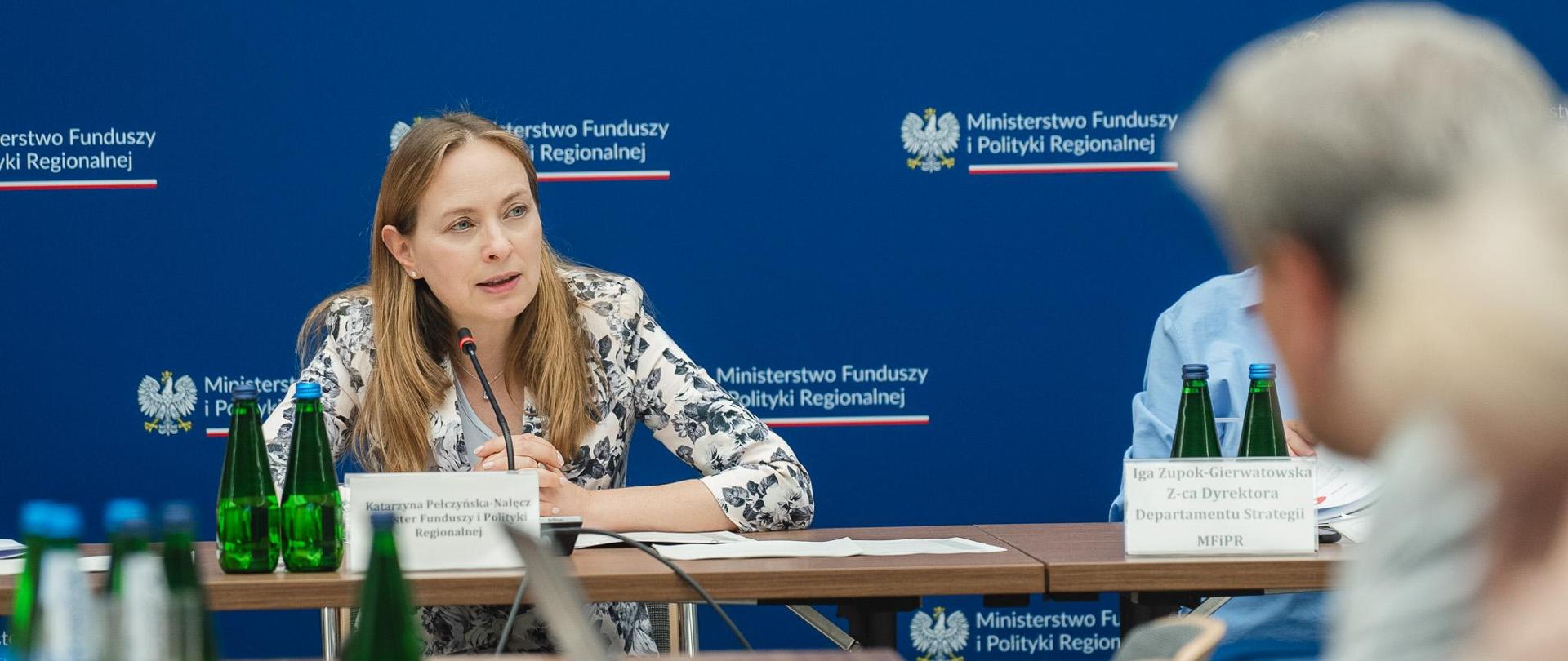Minister Katarzyna Pełczyńska-Nałęcz siedzi przy stole i patrzy do przodu.