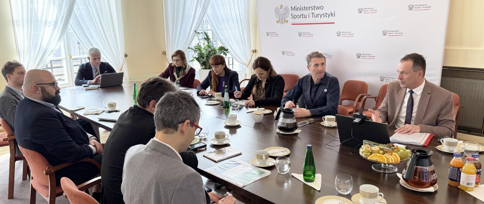 Piotr Borys na spotkaniu z branżą turystyczną w Ministerstwie Sportu i Turystyki na tle ścianki z logiem ministerstwa