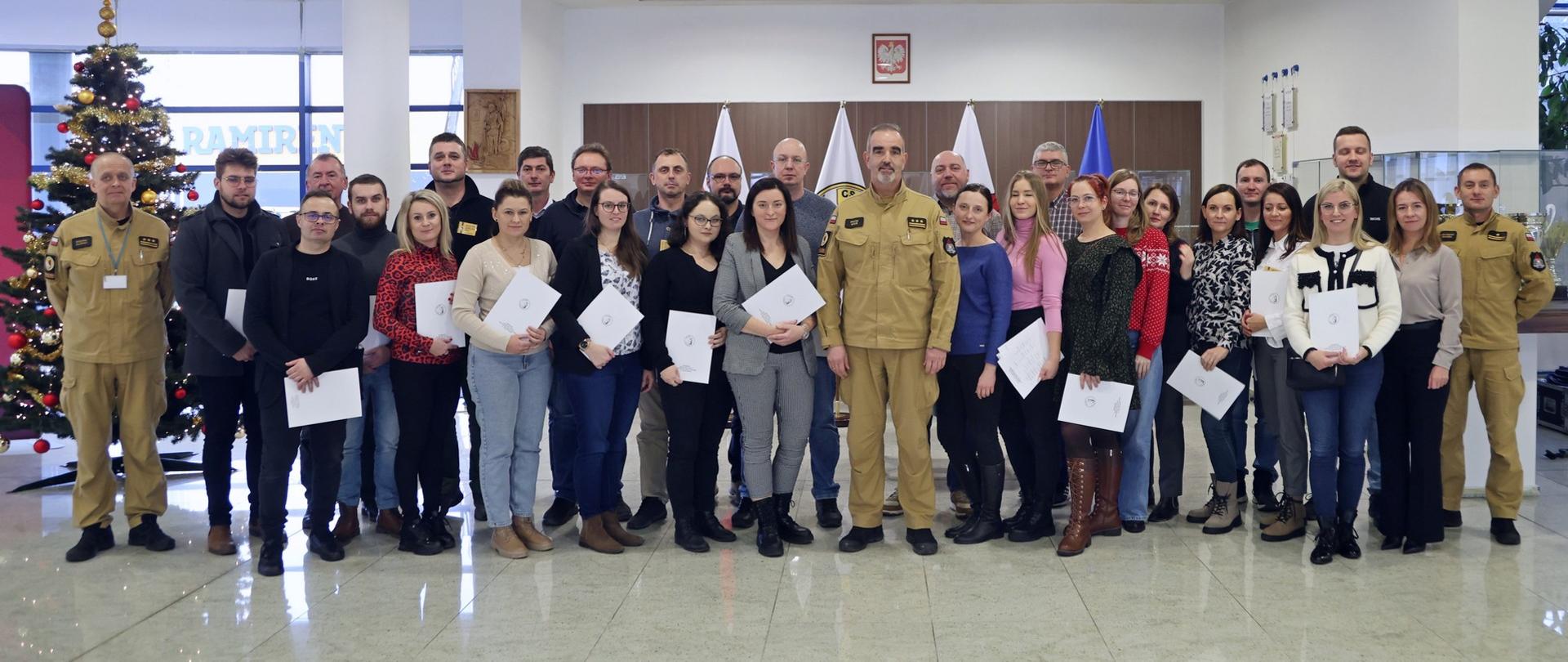 Pamiątkowe zdjęcie grupowe uczestników szkolenia inspektorów ochrony przeciwpożarowej (27 osób) w towarzystwie Zastępcy Komendanta Centralnej Szkoły PSP, kobiety oraz dwóch oficerów CS PSP