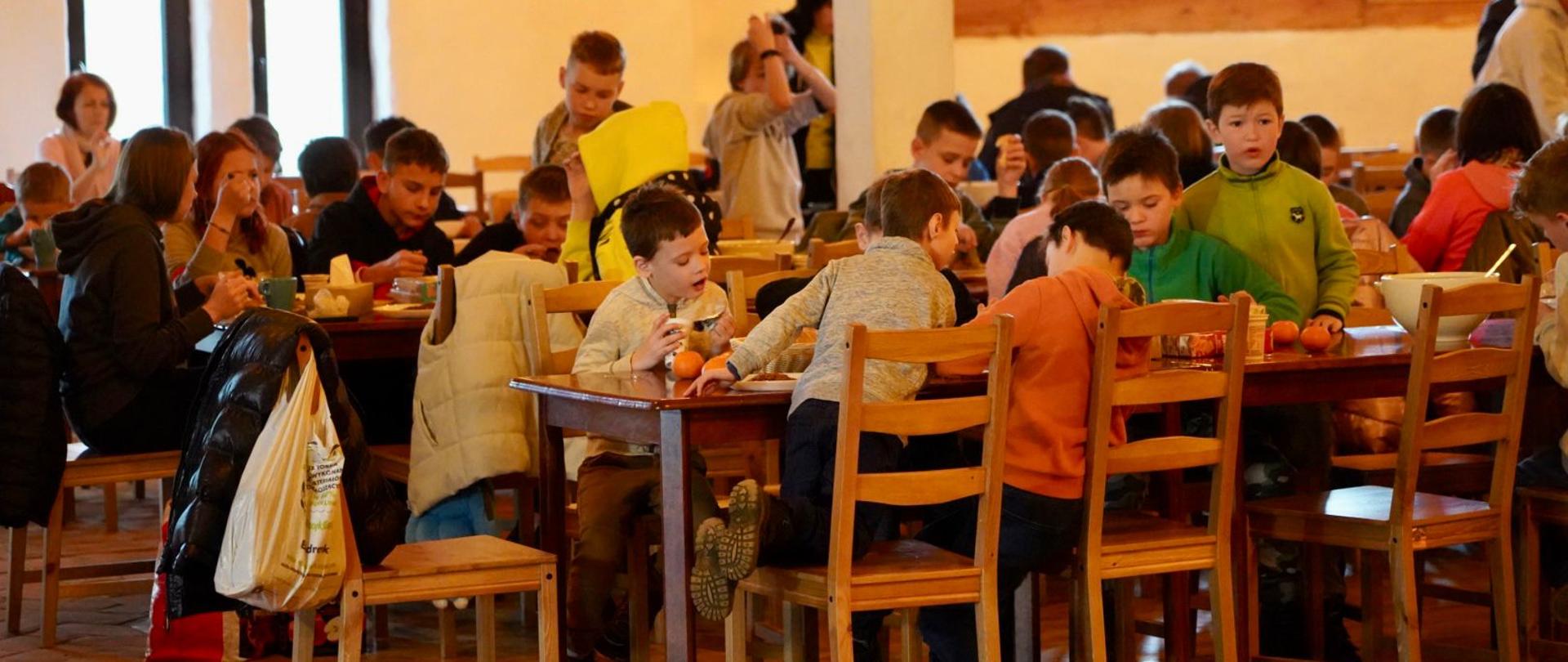 dzieci siedzą przy stołach i jedzą 