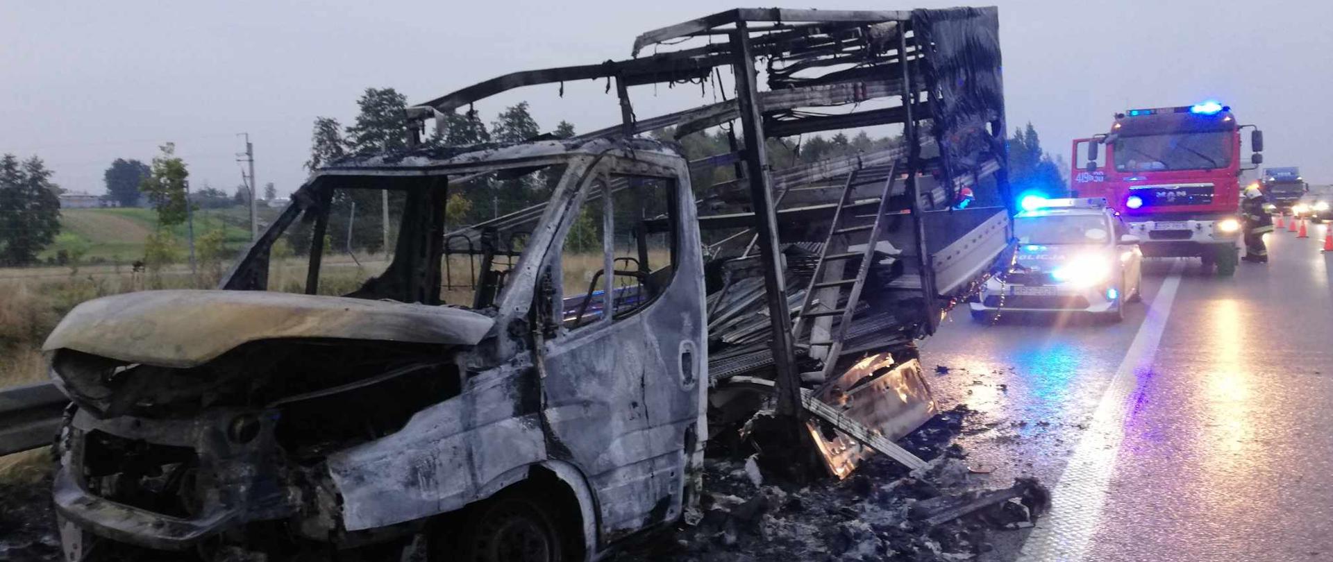 na pasie awaryjnym autostrady stoi całkowicie spalony samochód dostawczy marki Iveco za wrakiem samochód Policji jeszcze za nim samochód bojowy straży pożarnej, dalej widać również zakorkowaną autostradą czyli wiele samochodów stojących jeden za drugim