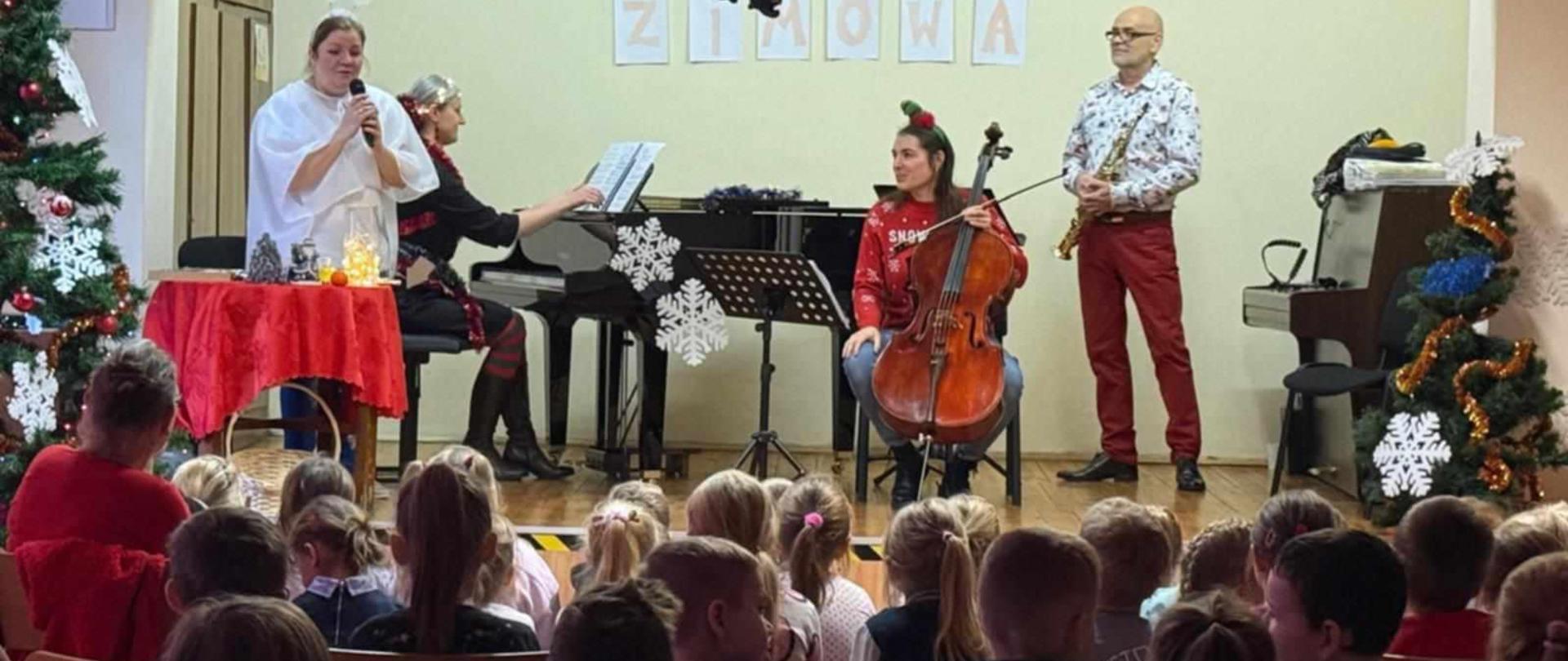 Dzieci siedzą przodem do sceny. Na scenie nauczyciele w strojach świątecznych oraz udekorowany fortepian.