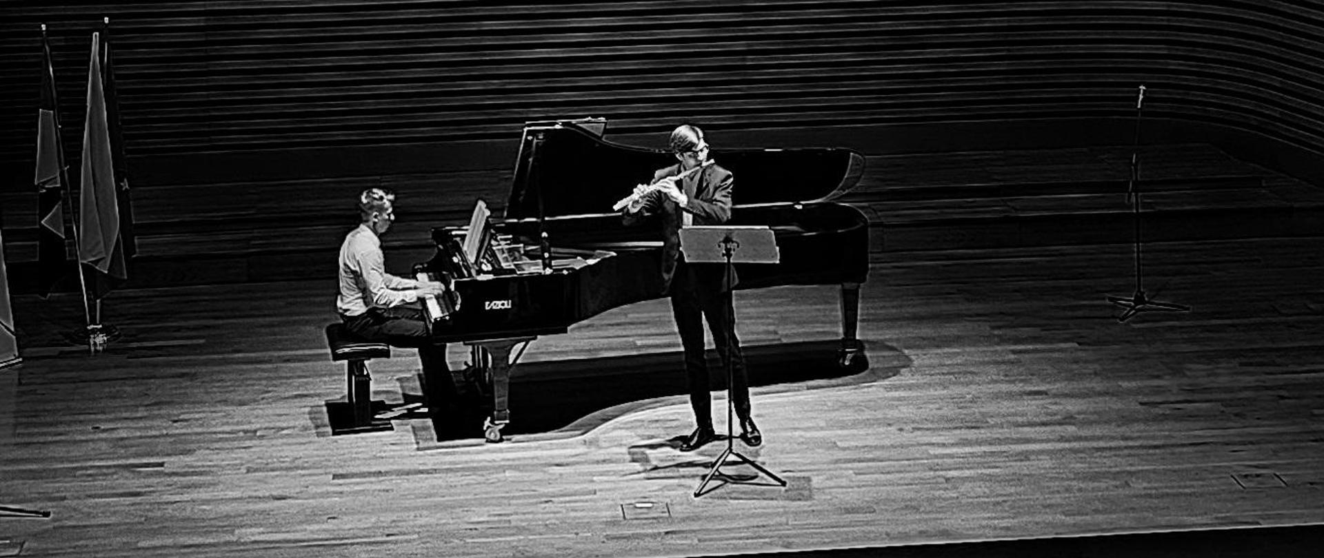 Na scenie pianista Michał Krupa gra na fortepianie Fazioli F308 orz flecista Rafał Jaworski, Wszystko w kolorach czerni i bieli. Widać głowy widzów.