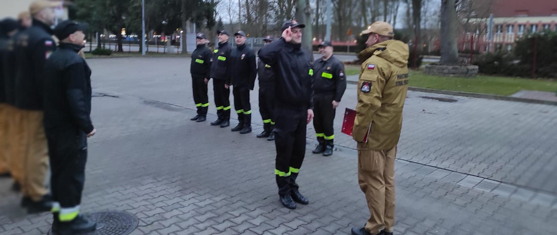 Strażacy stojący na zbiórce, mianowany strażak salutuje przed Komendantem