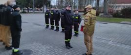 Strażacy stojący na zbiórce, mianowany strażak salutuje przed Komendantem