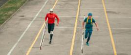 Na zdjęciu widocznych jest dwóch zawodników biegnących z drabinami hakowymi. 