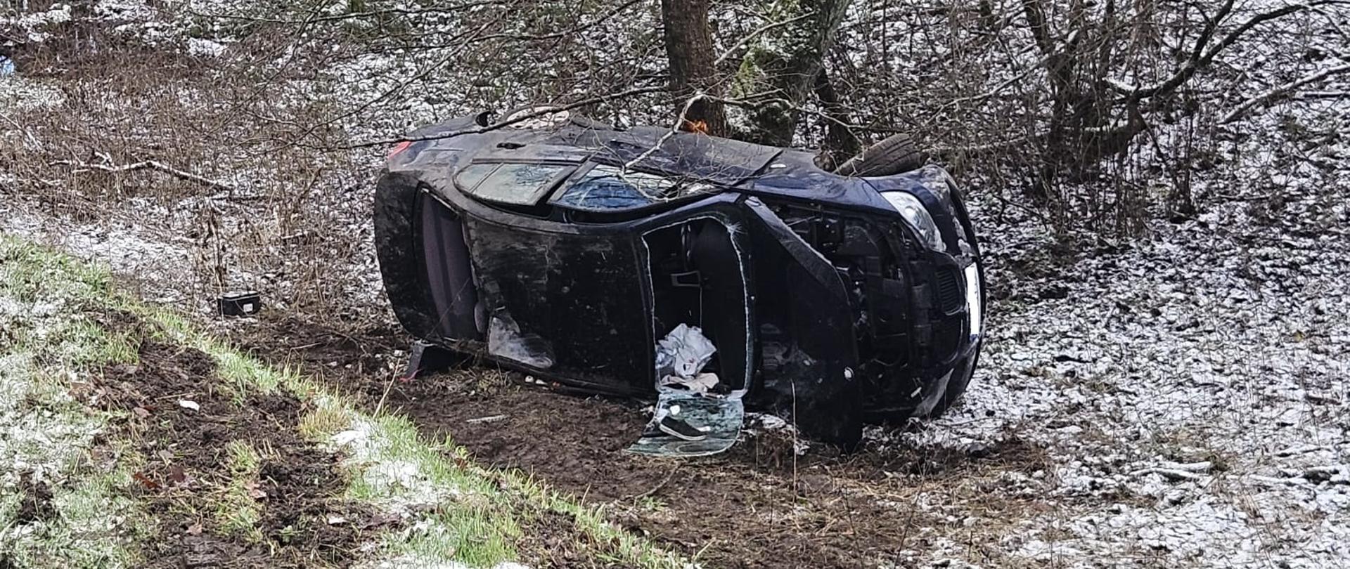 Auto czarne leżące na boku w zaśnieżonym rowie.