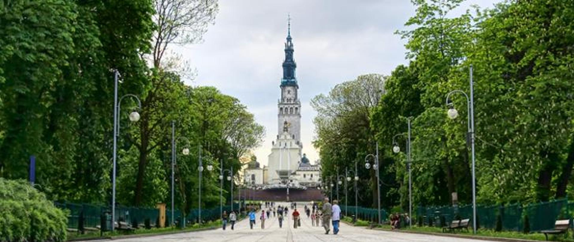 Na zdjęciu znajduje się kościół wśród drzew oraz ludzie idący do niego 