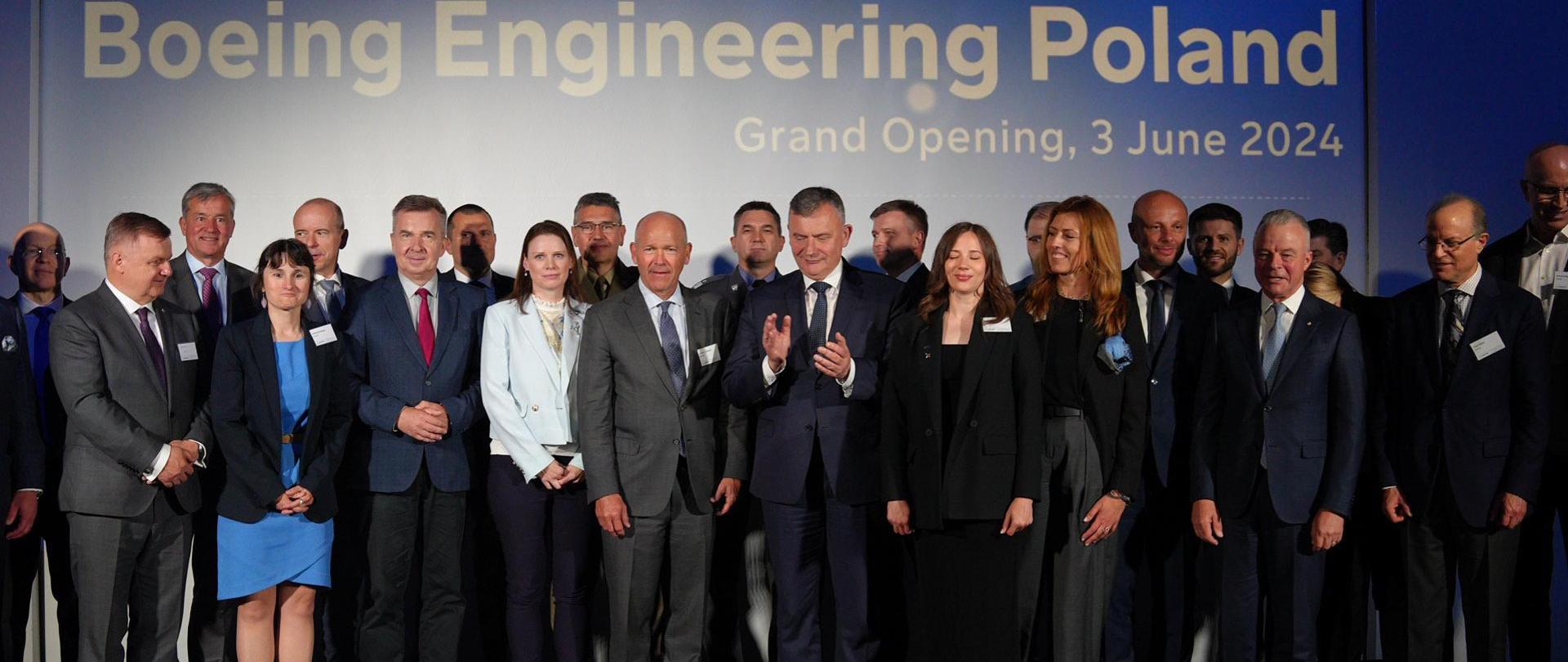 Zdjęcie zbiorowe, pod niebieską ścianą z napisem Boeing Engineering Poland stoi duża grupa osób.