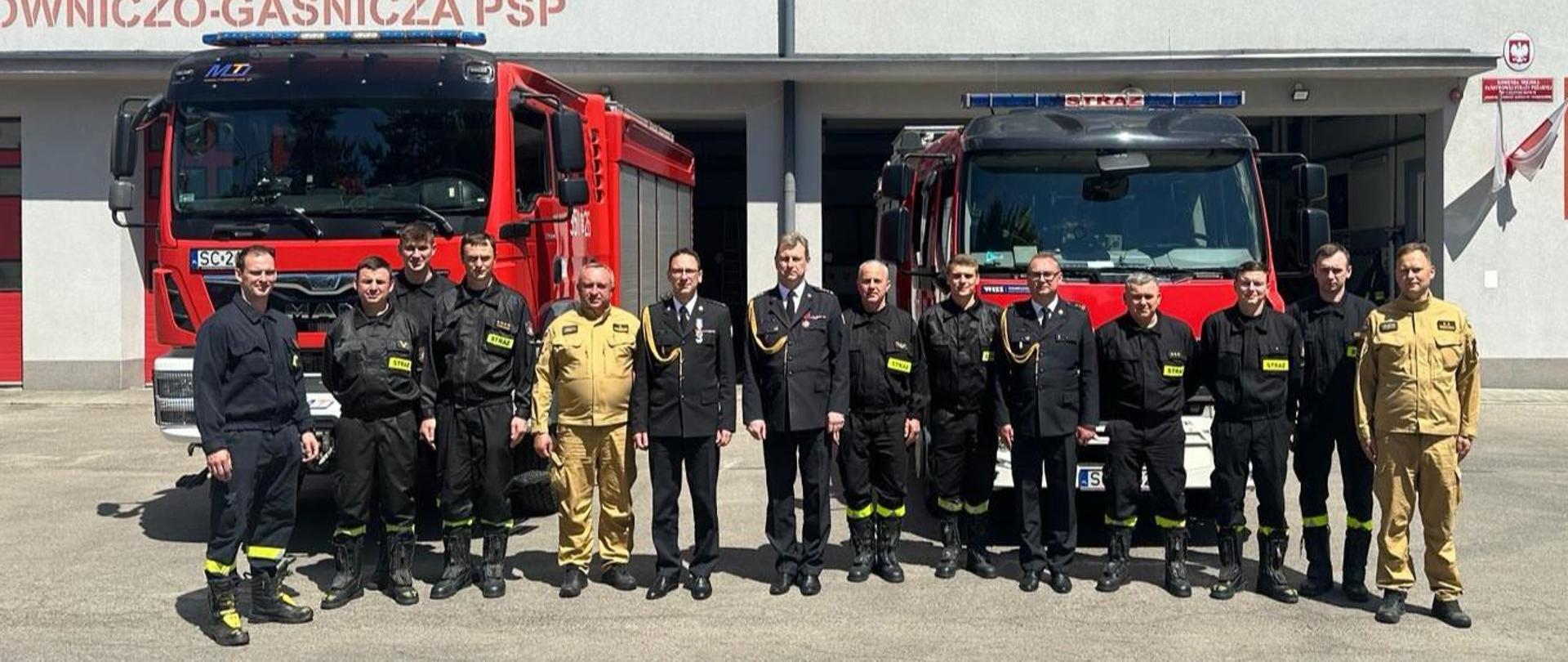 Zdjęcie grupowe strażaków Jednostki Ratowniczo - Gaśniczej numer 1 w Częstochowie podczas wizytacji Śląskiego Komendanta Wojewódzkiego Państwowej Straży Pożarnej. W tle samochody strażackie oraz budynek jednostki.