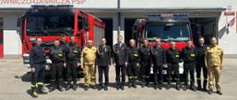 Zdjęcie grupowe strażaków Jednostki Ratowniczo - Gaśniczej numer 1 w Częstochowie podczas wizytacji Śląskiego Komendanta Wojewódzkiego Państwowej Straży Pożarnej. W tle samochody strażackie oraz budynek jednostki.