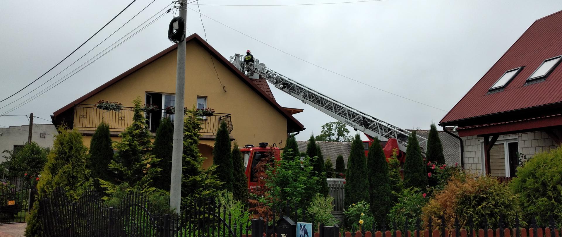 Budynek jednorodzinny w miejscowości Korczyn : prowadzenie akcji ratowniczo-gaśniczej na dachu budynku. Widać drabinę mechaniczną i strażaka pracującego nad dachem.