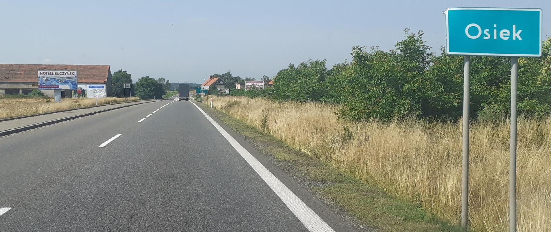 na zdjęciu widać drogę jednojezdniową oraz zieloną tablicę z nazwą miejscowości Osiek, w tle zabudowania