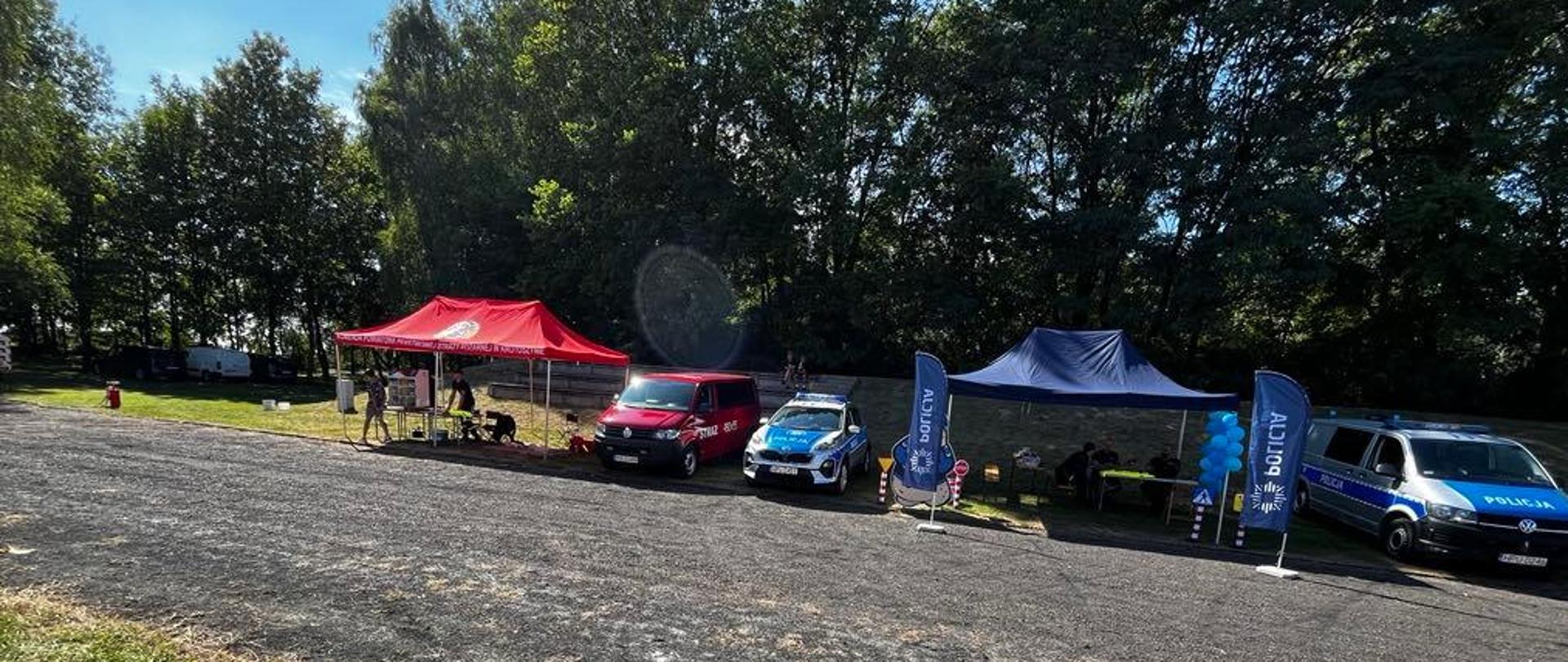 Na terenie stadionu gminnego w Rozdrażewie odbywają się dozynki gminne. Na zdjęciu stoisko strażackie oraz Policji wykonane z namiotów. Obok namiotów stoją samochody pożarnicze.