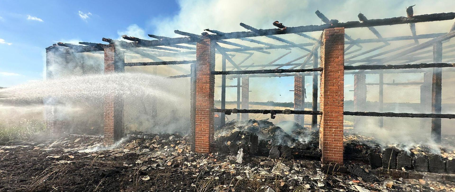 Zdjęcie przedstawia strażaków podczas gaszenia pożaru budynku gospodarczego
