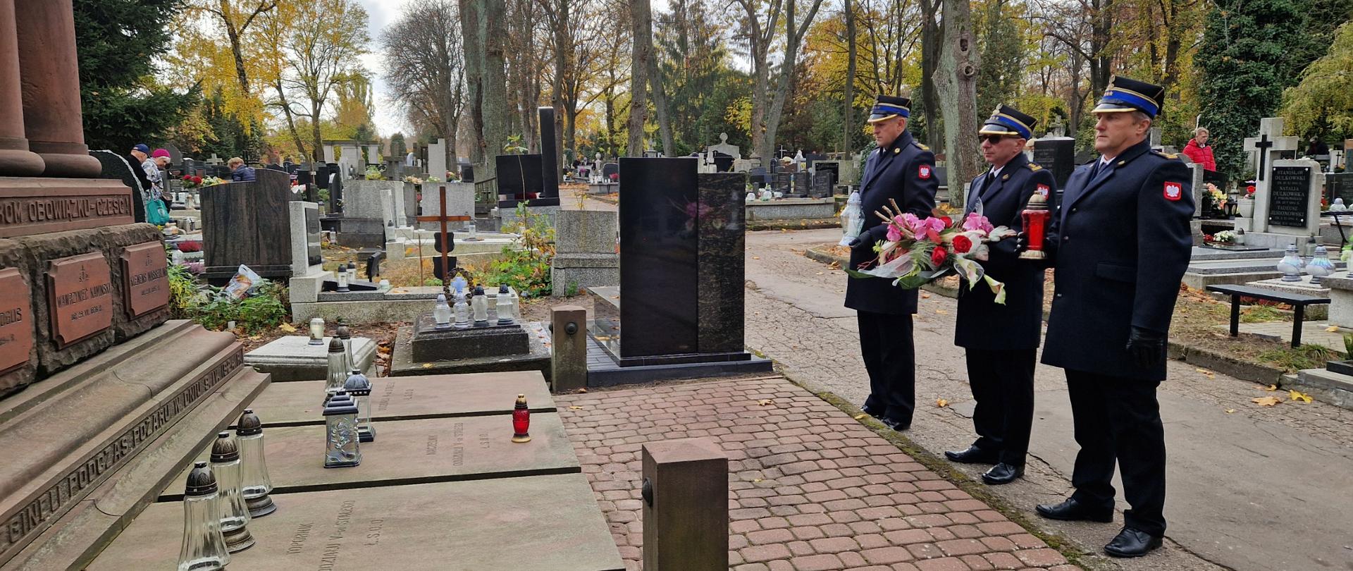 Komendanci stojący przed pomnikiem z kwiatami i zniczami